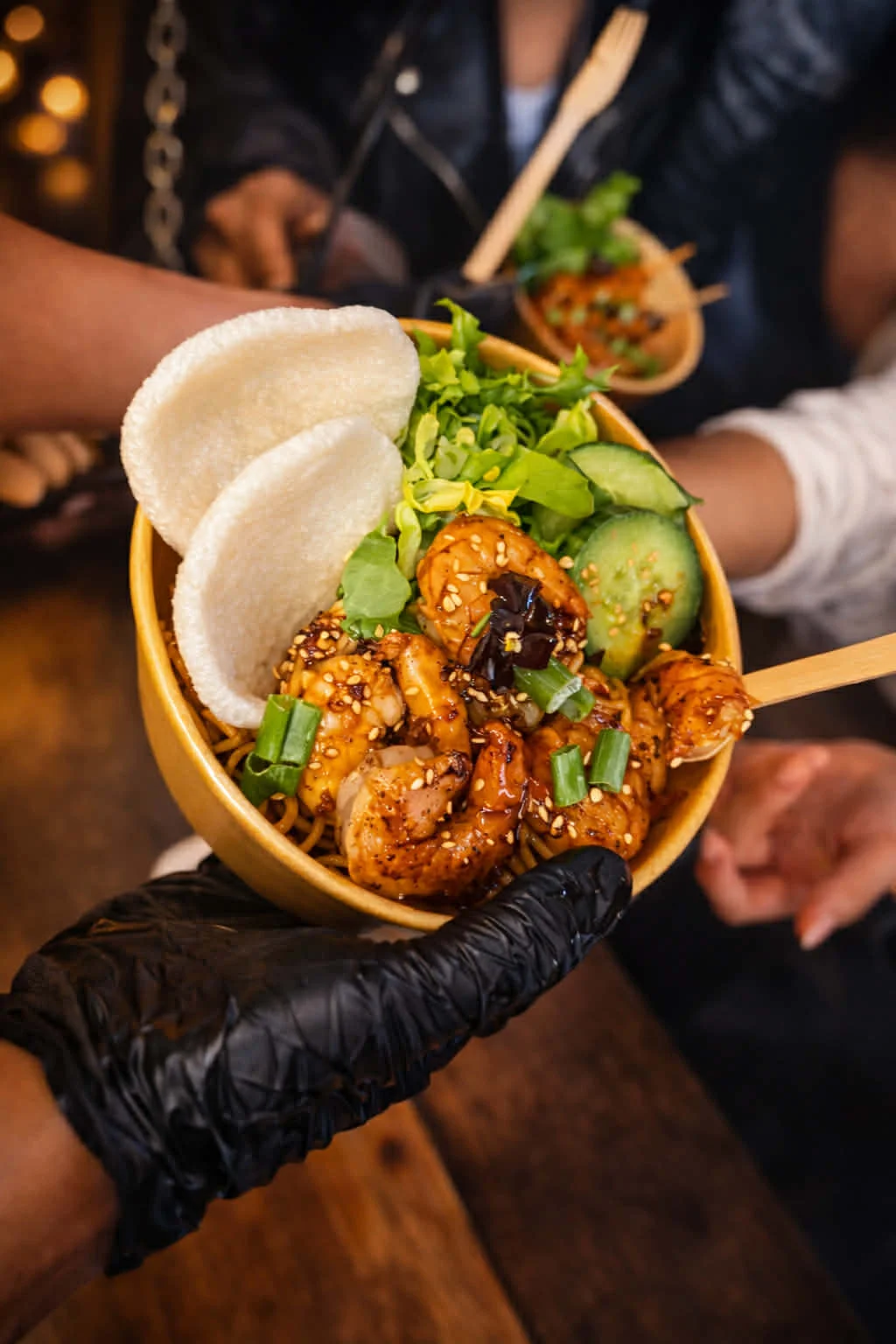 Bowl de crevettes caramélisées au sésame sur nouilles, servi avec concombre, salade et crackers, préparé par le food truck asiatique Soegito en Belgique