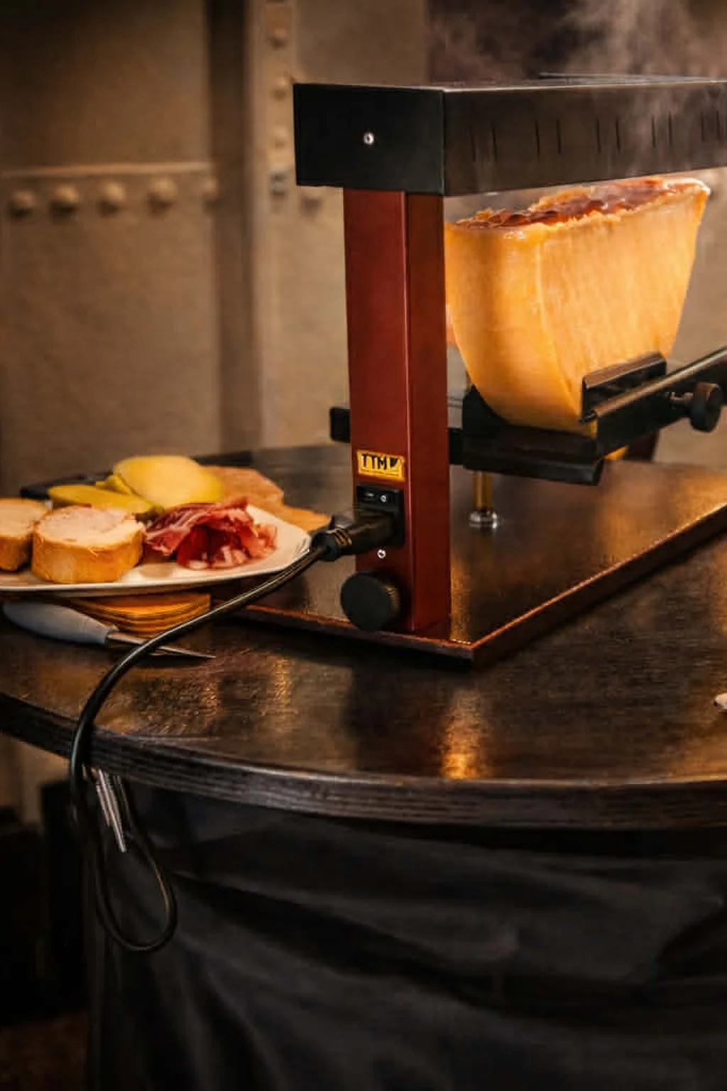Machine à raclette traditionnelle fumante avec charcuterie et pain, proposée dans le cadre du service horeca et traiteur événementiel de Soegito en Belgique